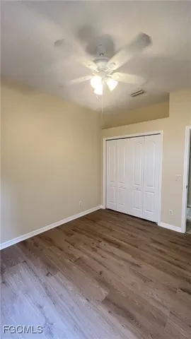 a view of an empty room with wooden floor and fan