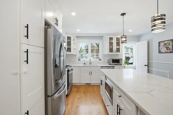 a kitchen with stainless steel appliances granite countertop a refrigerator a sink dishwasher a oven and white cabinets with wooden floor