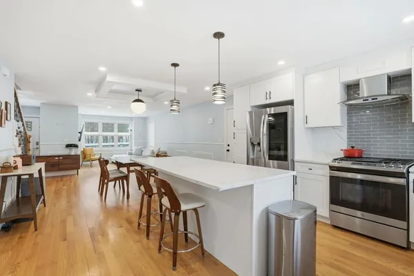 a kitchen with stainless steel appliances kitchen island granite countertop a stove a refrigerator a oven a dining table and chairs with wooden floor