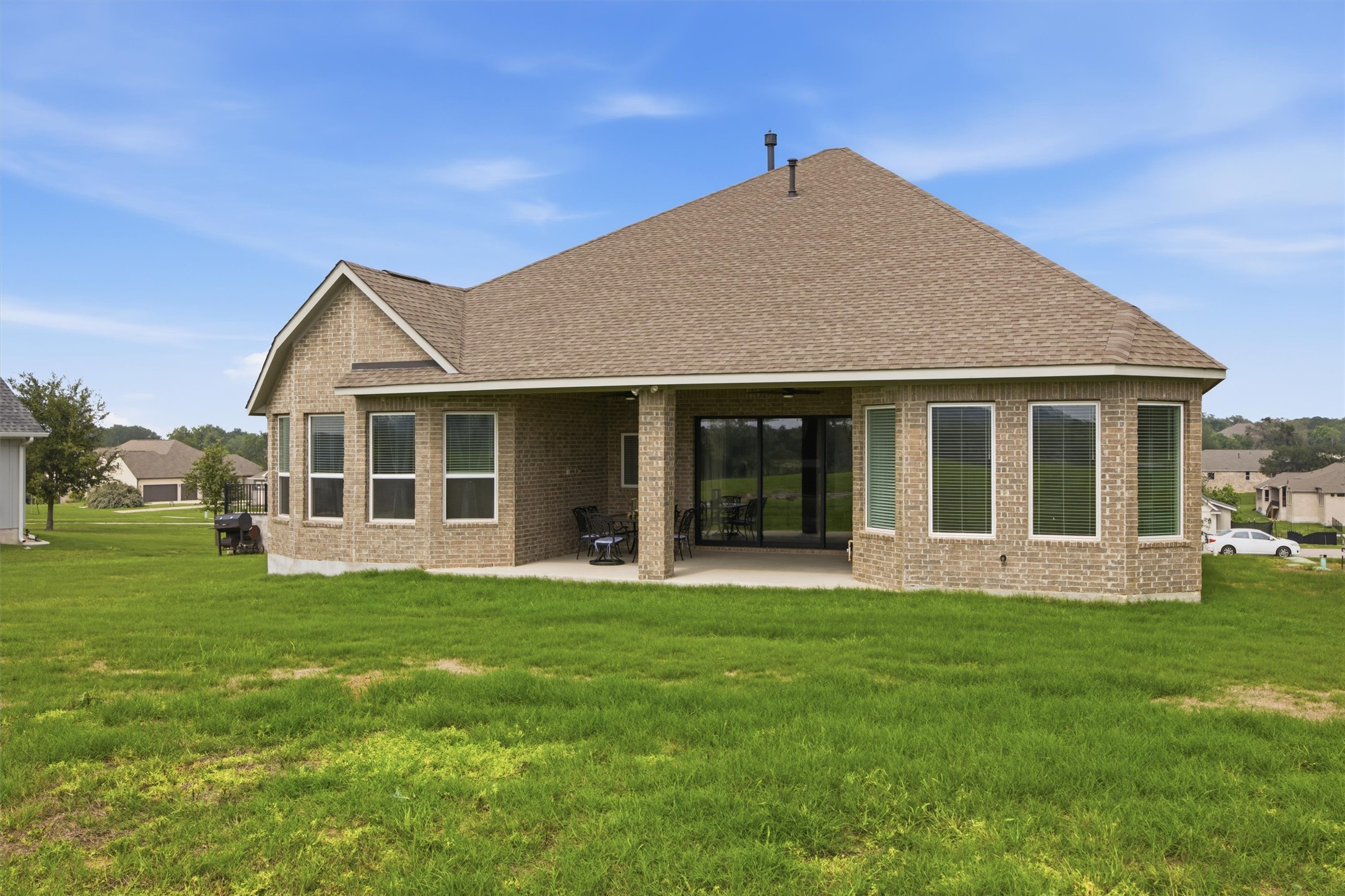 192 Raptor Beak Way Cedar Creek, TX 78612 - Photo 34 of 38 Expansive rear exterior featuring a covered patio, multiple large windows, a tan brick facade, and a shingle roof