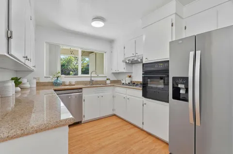 a kitchen with stainless steel appliances granite countertop a refrigerator a sink a stove a washer and dryer with wooden floor