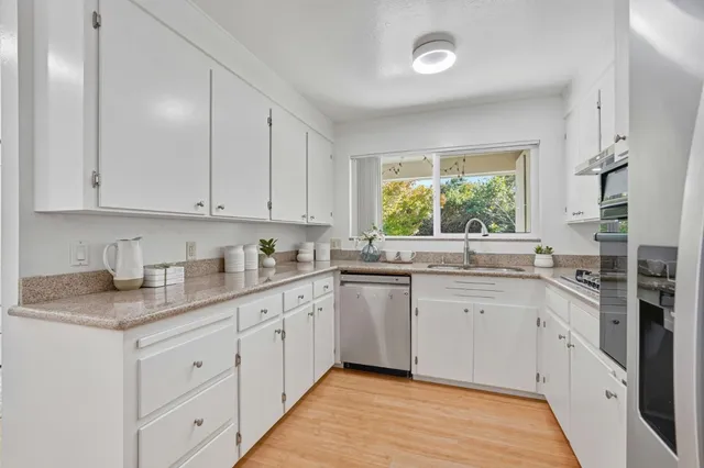a kitchen with granite countertop white cabinets white appliances a sink and a window