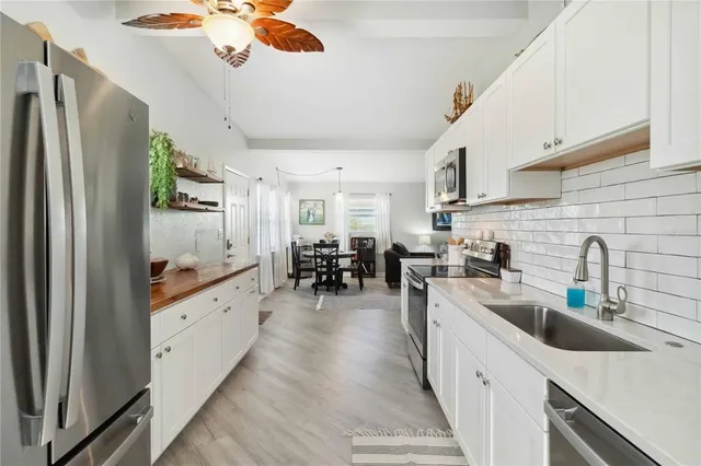a kitchen with stainless steel appliances a refrigerator a sink dishwasher a stove and white cabinets with wooden floor