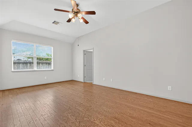 an empty room with wooden floor chandelier fan and windows