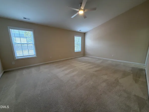 an empty room with chandelier fan and windows