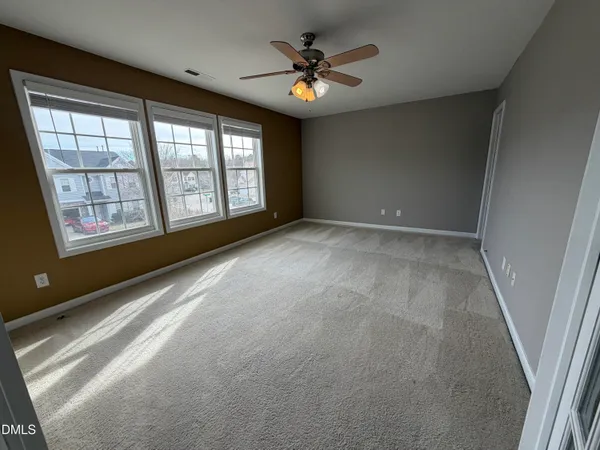 an empty room with chandelier fan and windows