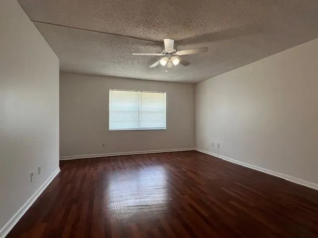 an empty room with wooden floor chandelier fan and windows