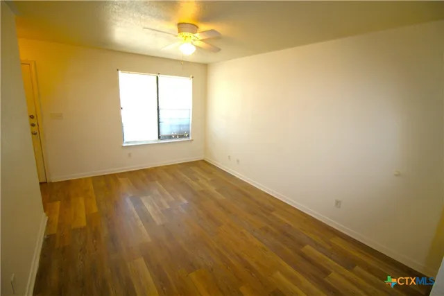 a view of an empty room with wooden floor and a window