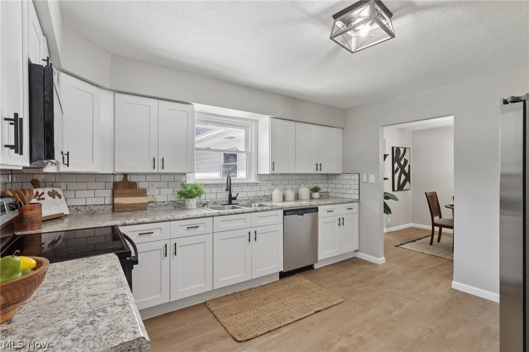 7412 Hopkins Road Mentor, OH 44060 - Photo 13 of 36 Kitchen with light wood-type flooring, stainless steel appliances, white cabinets, backsplash, and a textured ceiling