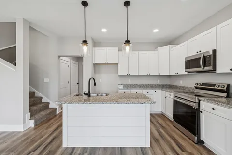 a kitchen with stainless steel appliances granite countertop a sink a stove a refrigerator and white cabinets with wooden floor