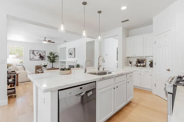 a kitchen with a sink dishwasher and white cabinets with wooden floor