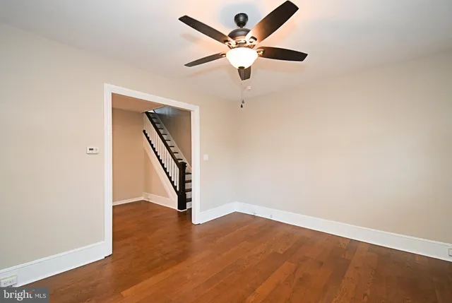 an empty room with wooden floor ceiling fan and stairs