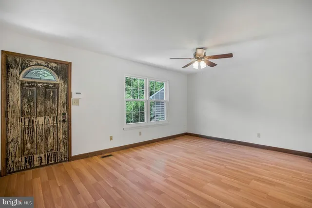 an empty room with wooden floor chandelier fan and windows