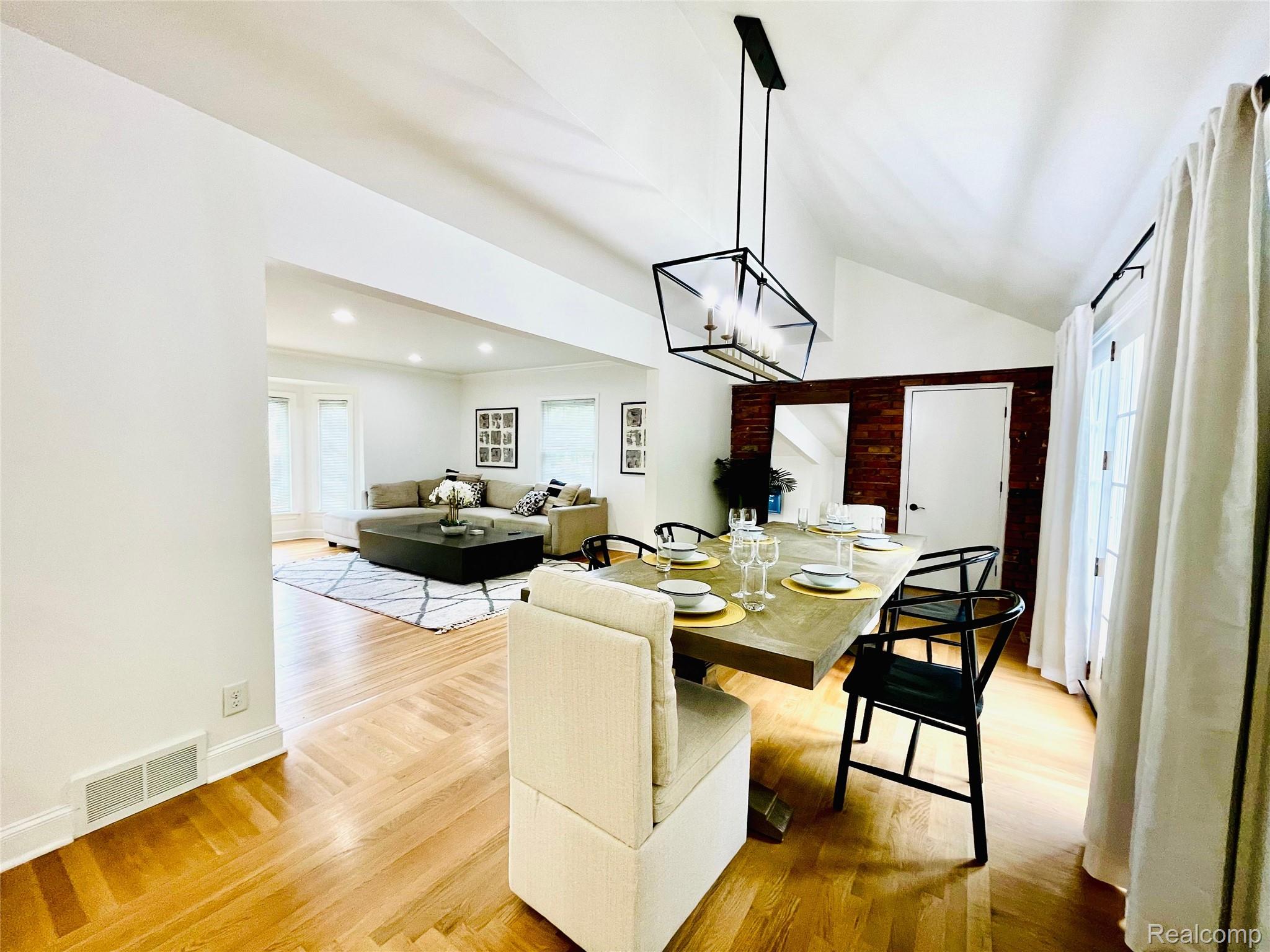 60 Devon Road Bloomfield Hills, MI 48302 - Photo 16 of 50 Vaulted ceiling dining area featuring a linear chandelier with clear glass shades, herringbone wood-finish flooring, and a brick accent wall with a white paneled door