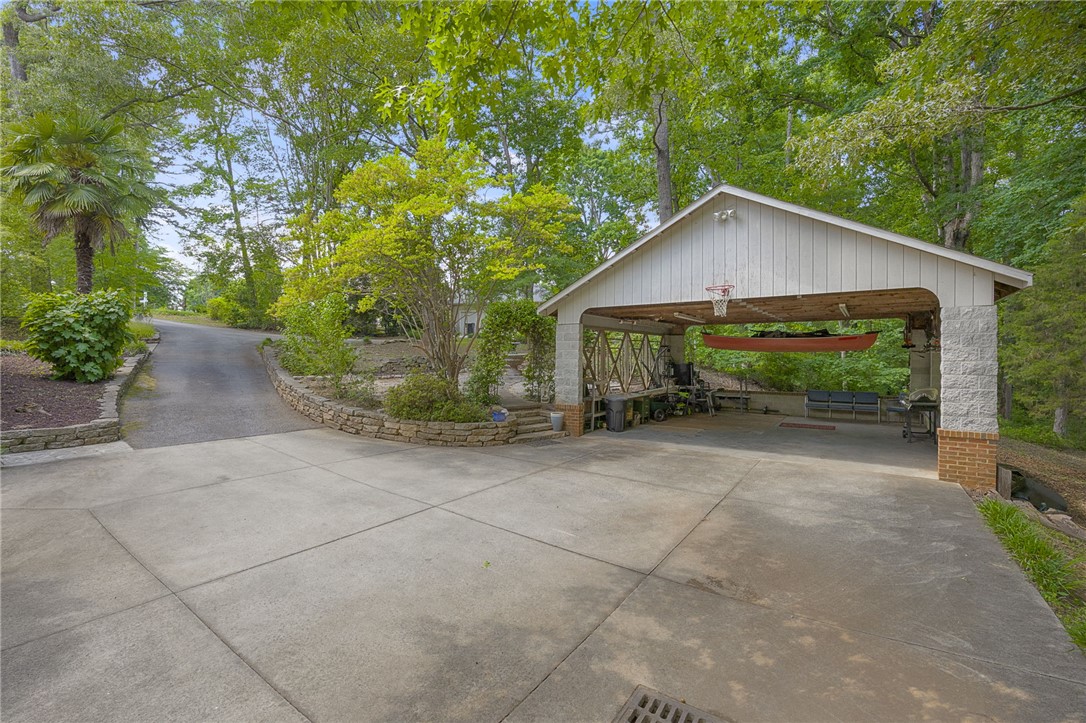 218 Northridge Drive Anderson, SC 29621 - Photo 43 of 50 A spacious concrete driveway leads to a sheltered carport with a basketball hoop, surrounded by mature trees and lush landscaping.