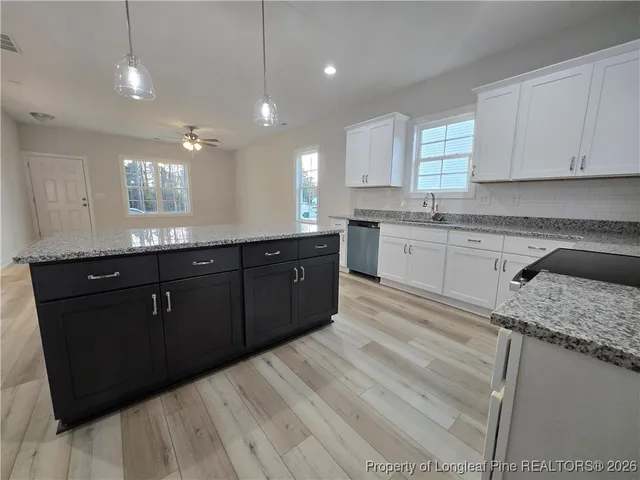 a large kitchen with granite countertop a sink dishwasher a stove and white cabinets
