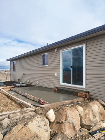 1510 South Lawrence Road Huntington, UT 84528 - Photo 13 of 16 Exterior featuring tan horizontal siding, a sliding glass door, a newly poured concrete patio, and a rock retaining wall
