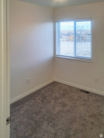 1510 South Lawrence Road Huntington, UT 84528 - Photo 6 of 16 Corner room featuring a window with horizontal blinds, neutral wall paint, gray textured carpeting, white baseboards, and a ceiling light fixture