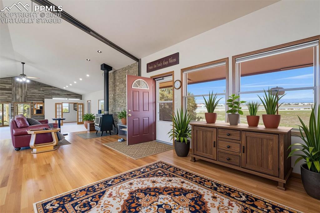 2550 Slocum Road Peyton, CO 80831 - Photo 3 of 50 virtually staged Open concept interior featuring hardwood flooring, a vaulted ceiling, and a stone accent wall with a wood-burning stove
