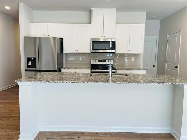 a kitchen with stainless steel appliances granite countertop a stove a refrigerator a sink and white cabinets