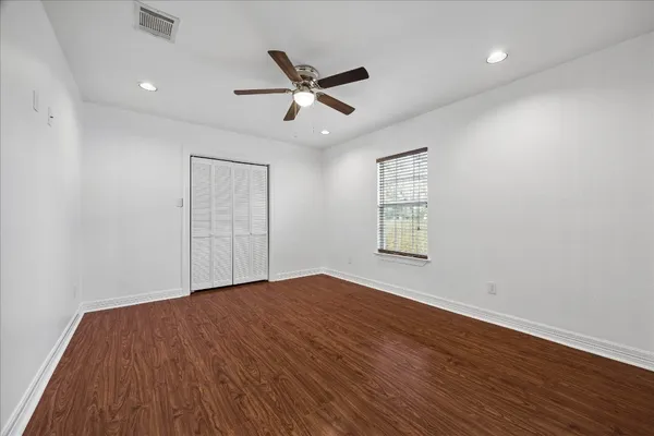 an empty room with wooden floor ceiling fan and windows