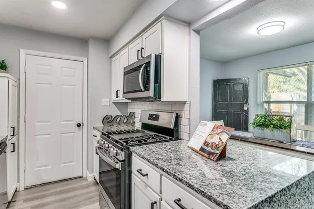 a kitchen with stainless steel appliances granite countertop a stove top oven a sink dishwasher and a microwave with wooden floor