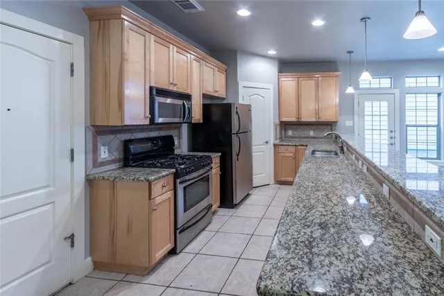 a kitchen with stainless steel appliances granite countertop a refrigerator a stove top oven and a sink