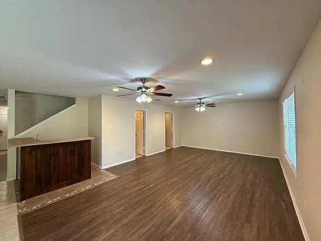 a view of an empty room with wooden floor and a ceiling fan