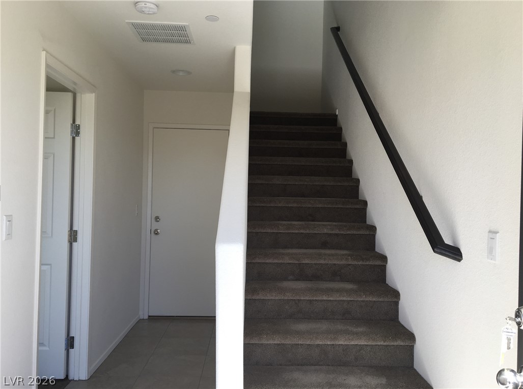 4650 Ranch House Road, Unit 9 North Las Vegas, NV 89031 - Photo 3 of 13 A welcoming entryway features tile flooring, leading to a staircase with carpeted steps and a dark handrail.