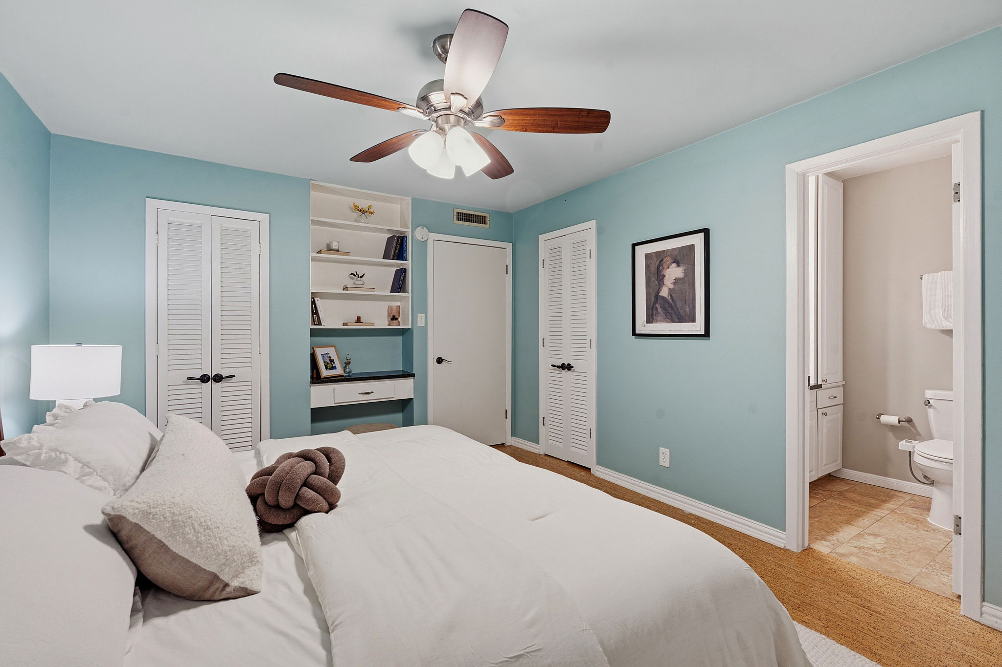 1210 Windsor Road, Unit 104 Austin, TX 78703 - Photo 18 of 29 A well-lit bedroom offers built-in shelving, providing both storage and display space, with convenient access to a private bathroom.