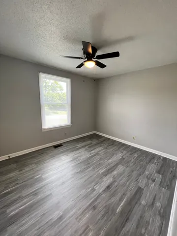 an empty room with wooden floor ceiling fan and windows