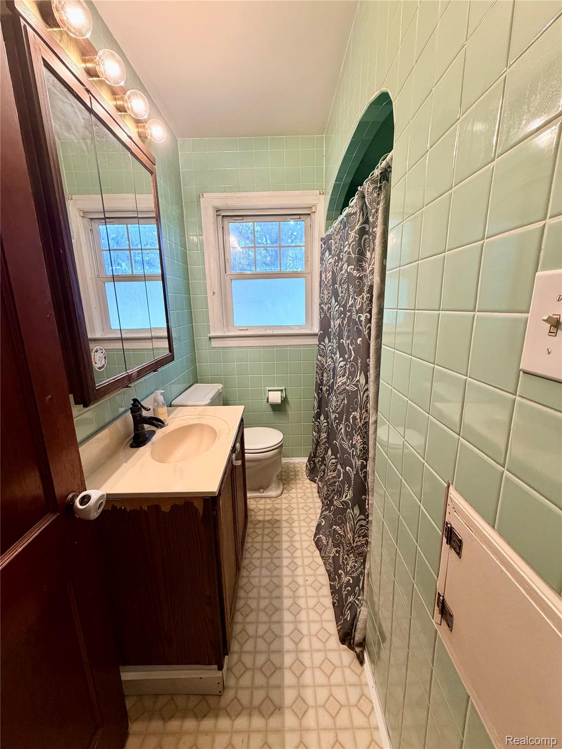 3840 East Dunbar Road Monroe, MI 48161 - Photo 28 of 38 Bathroom featuring light green tiled walls, a window with natural light, a dark wood-finish vanity with an integrated sink, a toilet, and patterned vinyl flooring