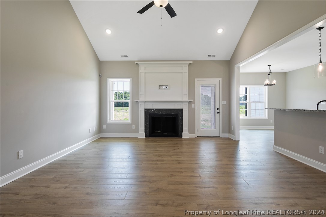 175 Spring Branch Road Tar Heel, NC 28392 - Photo 12 of 50 an empty room with wooden floor a ceiling fan a fireplace and windows