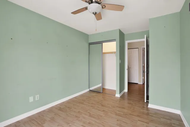 an empty room with wooden floor and way to kitchen