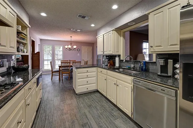 a kitchen with stainless steel appliances kitchen island granite countertop a stove a sink and white cabinets with wooden floor
