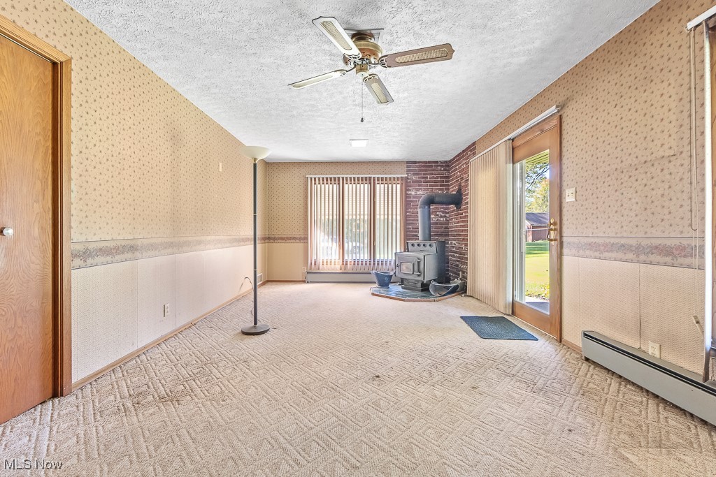 1165 Homeworth Road Alliance, OH 44601 - Photo 10 of 36 Carpeted spare room featuring a baseboard heating unit, a textured ceiling, a wood stove, and plenty of natural light