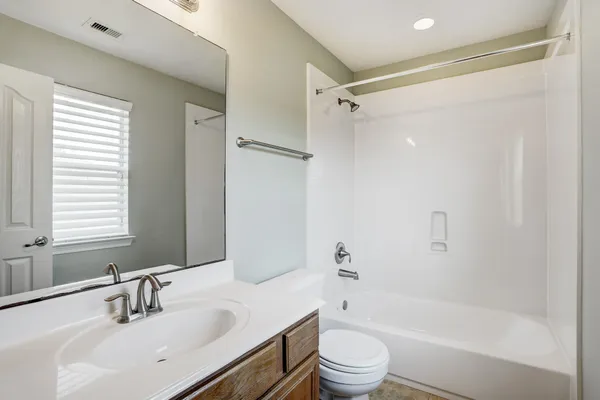 a bathroom with a bathtub shower sink vanity mirror and toilet