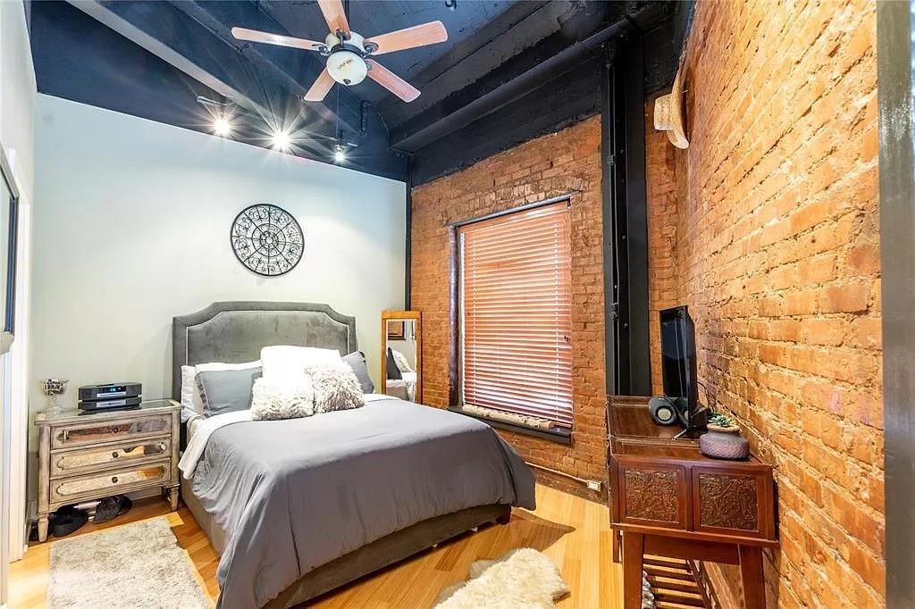 910 Houston Street, Unit 604 Fort Worth, TX 76102 - Photo 13 of 14 Bedroom featuring brick wall, wood finished floors, and ceiling fan