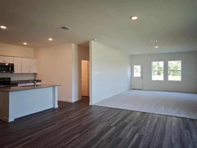 a view of a kitchen and an empty room with wooden floor and windows