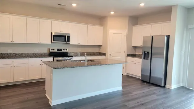 a kitchen with stainless steel appliances granite countertop a refrigerator a sink a stove a microwave and white cabinets