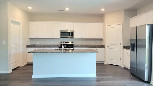 a kitchen with stainless steel appliances granite countertop a refrigerator a sink a stove a microwave and white cabinets