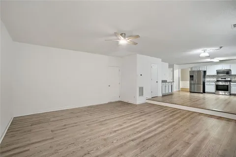 a view of empty room with wooden floor and kitchen view