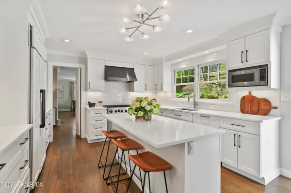 a kitchen with stainless steel appliances granite countertop a stove top oven a refrigerator a sink and a dining table with wooden floor