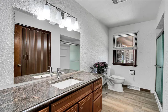 a bathroom with a granite countertop sink a toilet a mirror and shower