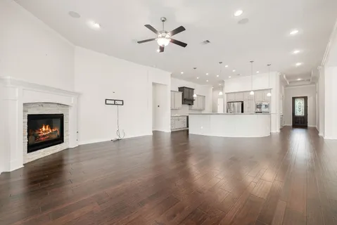 a view of an empty room and kitchen with fireplace ceiling fan
