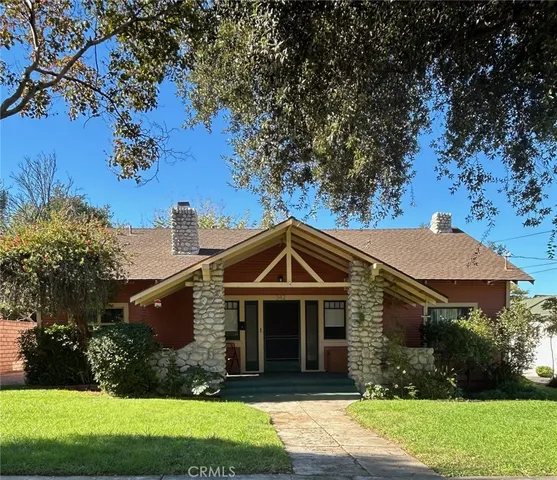 a view of a house with a yard plants and large tree