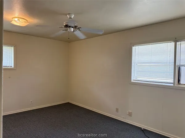 an empty room with a chandelier fan and windows