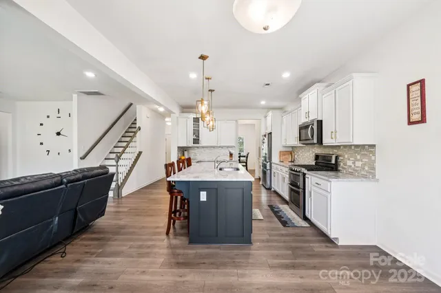 a large white kitchen with wooden floor and stainless steel appliances