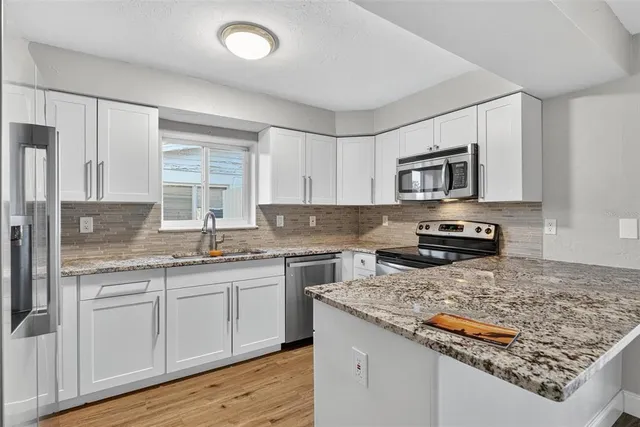 a kitchen with stainless steel appliances granite countertop a stove top oven a sink dishwasher and a microwave oven on the wooden floor