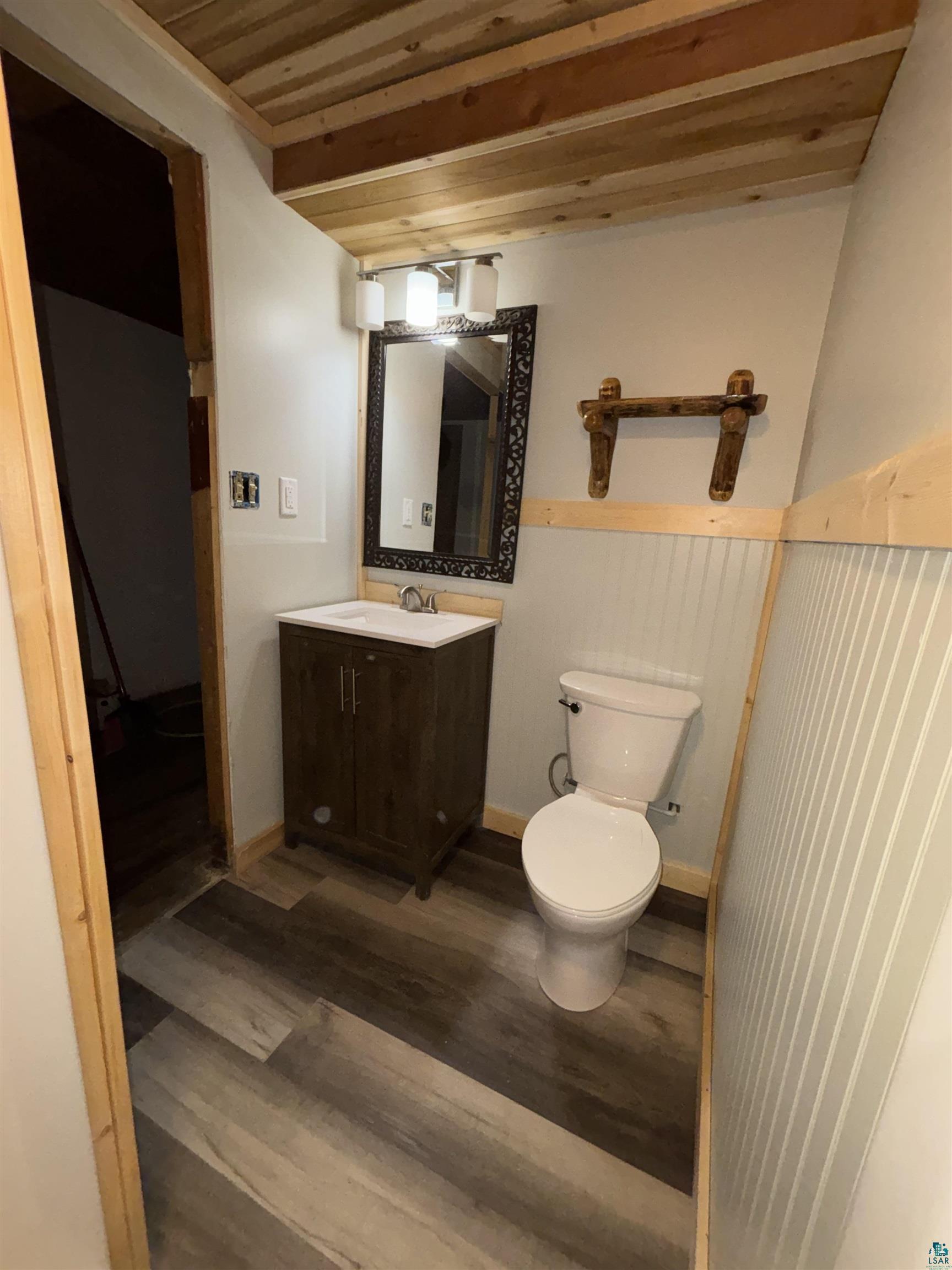 444 Fernberg Road, Unit 11 Ely, MN 55731 - Photo 19 of 19 Bathroom featuring a dark wood-finish vanity with a white countertop, an ornate framed mirror, and a three-light vanity fixture